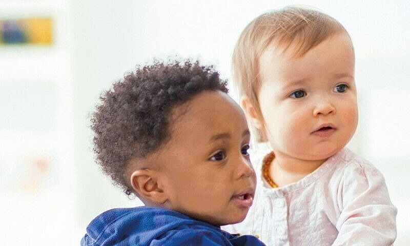 Das Bild zeigt zwei Kleinkinder, ein Mädchen und ein Junge, die Ihren Blick zum rechten Bildrand richten.