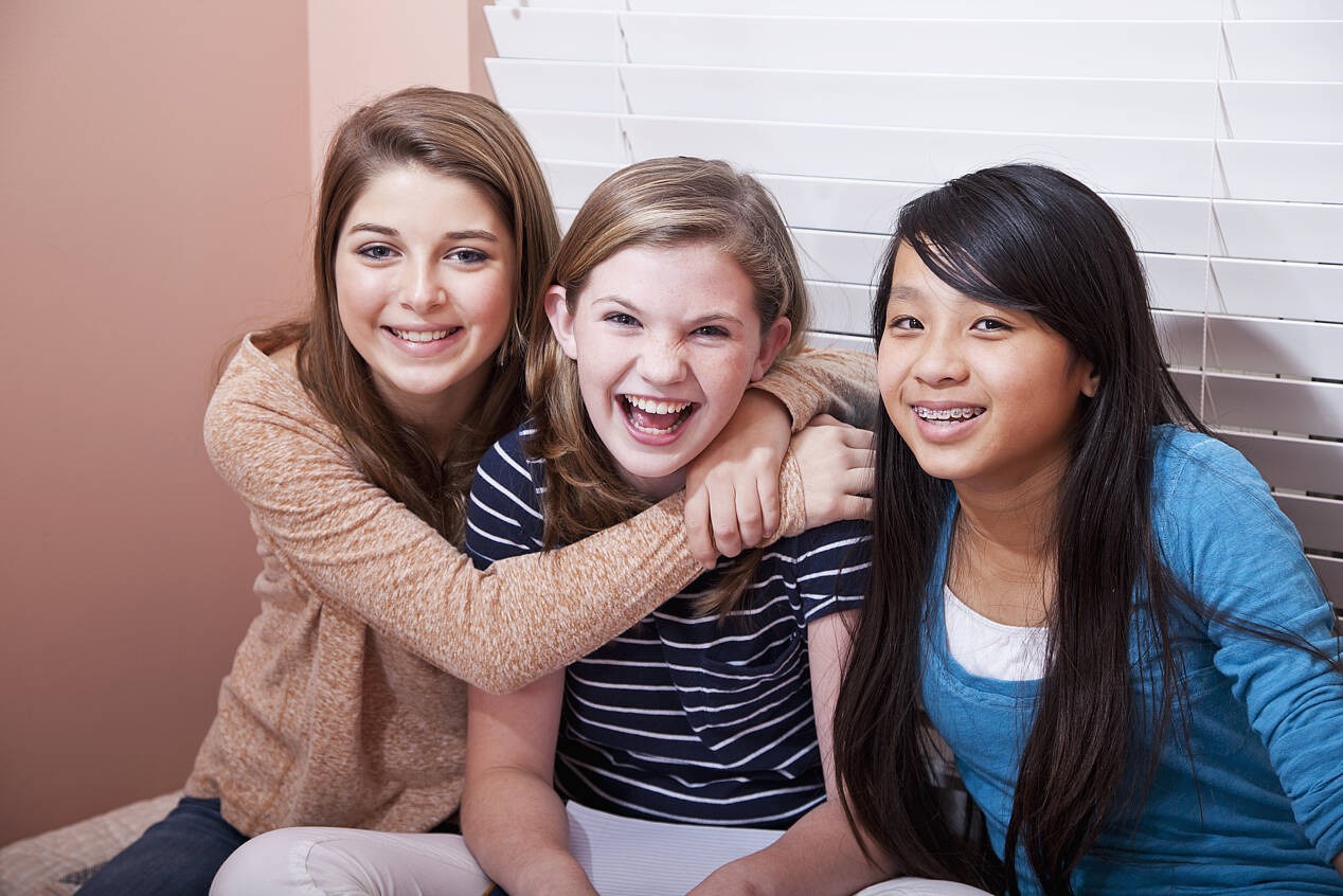 Drei weibliche Jugendliche sitzen lachend in einem Zimmer