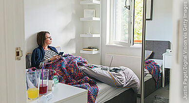 Frau zu Hause im Bett mit Laptop und Smartphone in der Hand