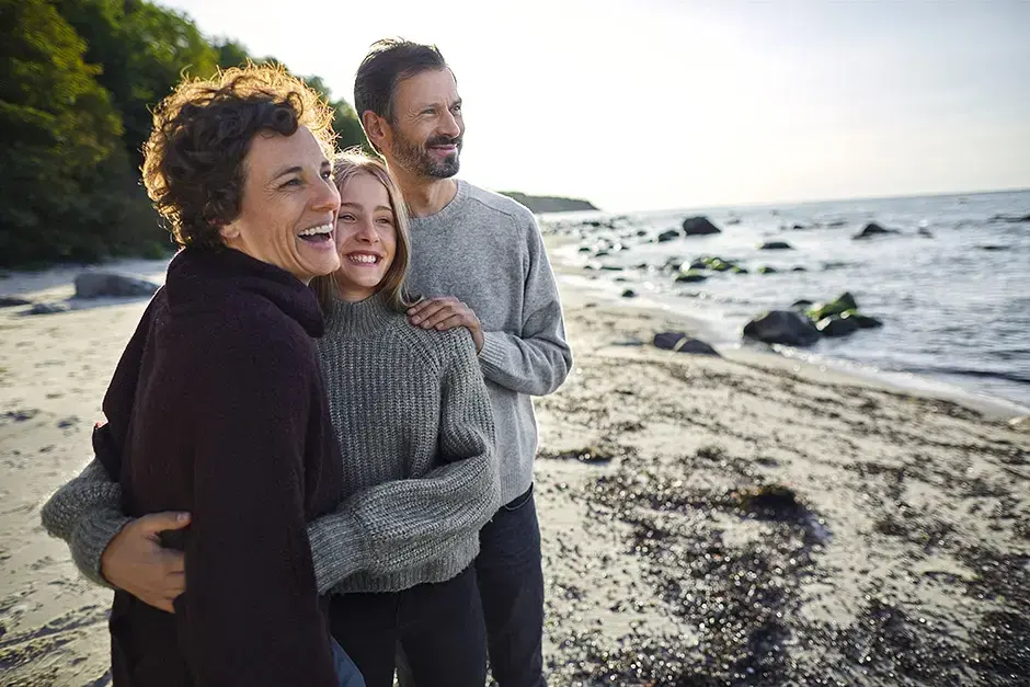 Drei Personen stehend lachend am Strand