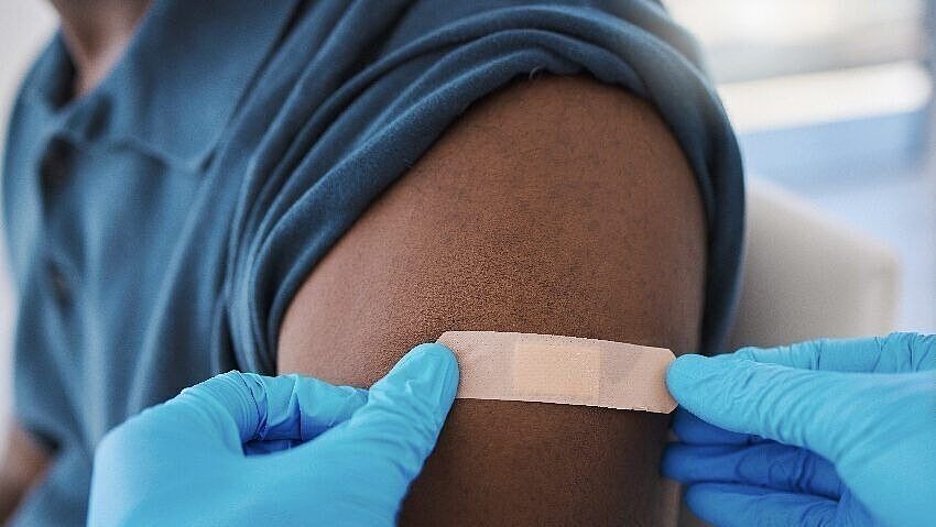 Jemand klebt ein Pflaster auf den Oberarm einer Person