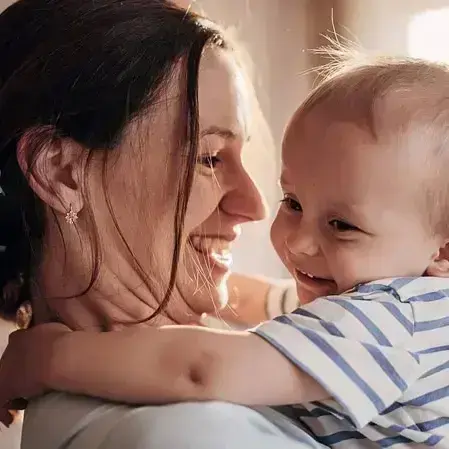 Frau hält ein Baby im Arm, beide lachen sich an