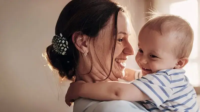 Frau hält ein Baby im Arm, beide lachen sich an