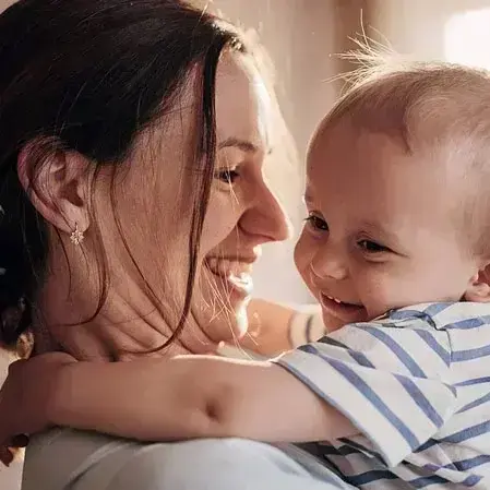 Frau hält ein Baby im Arm, beide lachen sich an