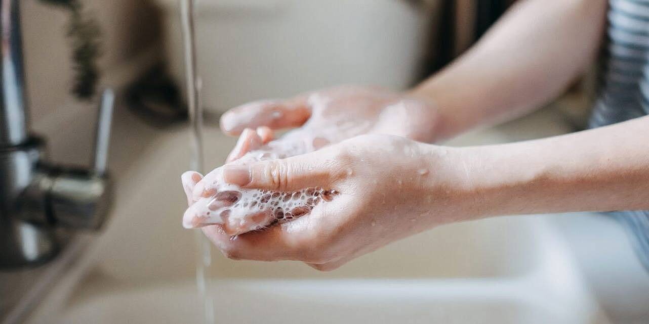 Eine Person steht am Waschbecken und wäscht sich die Hände. Man sieht nur die Händer und Arme.