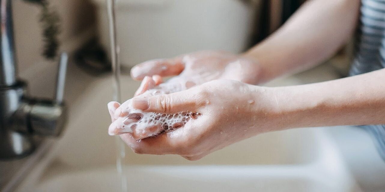 Eine Person steht am Waschbecken und wäscht sich die Hände. Man sieht nur die Händer und Arme.