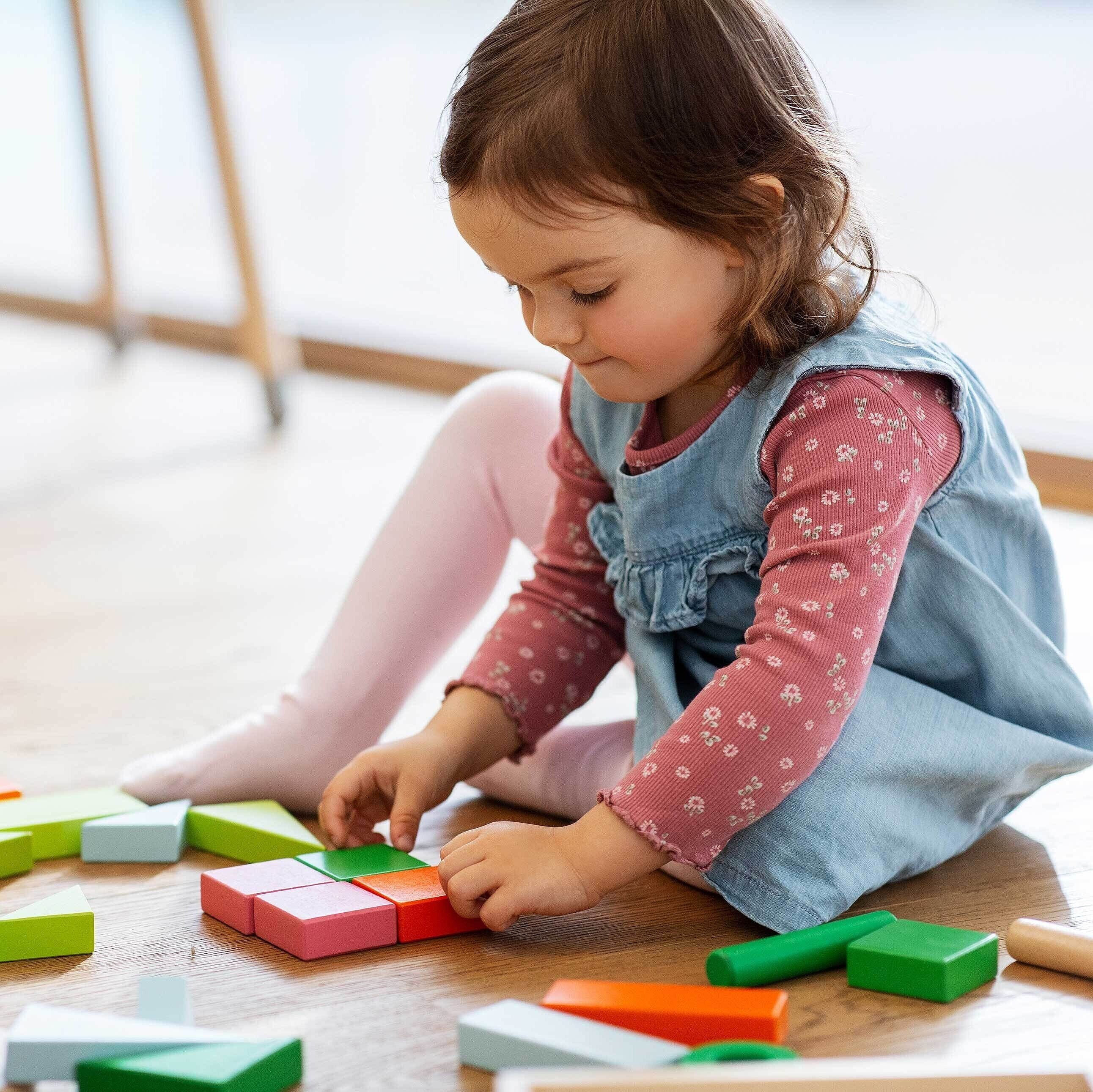 Mädchen spielt auf dem Boden mit Holzspielzeug