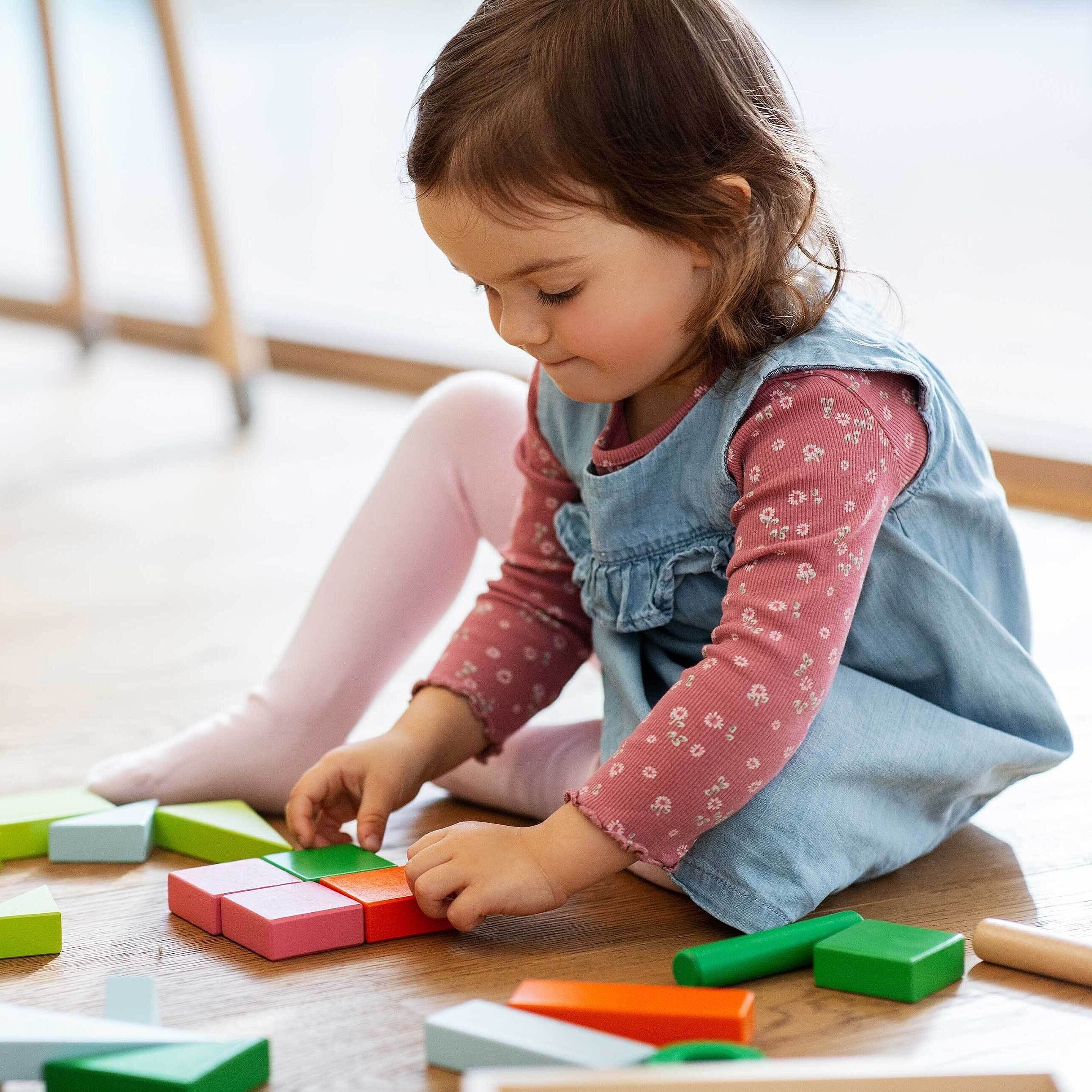 Mädchen spielt auf dem Boden mit Holzspielzeug