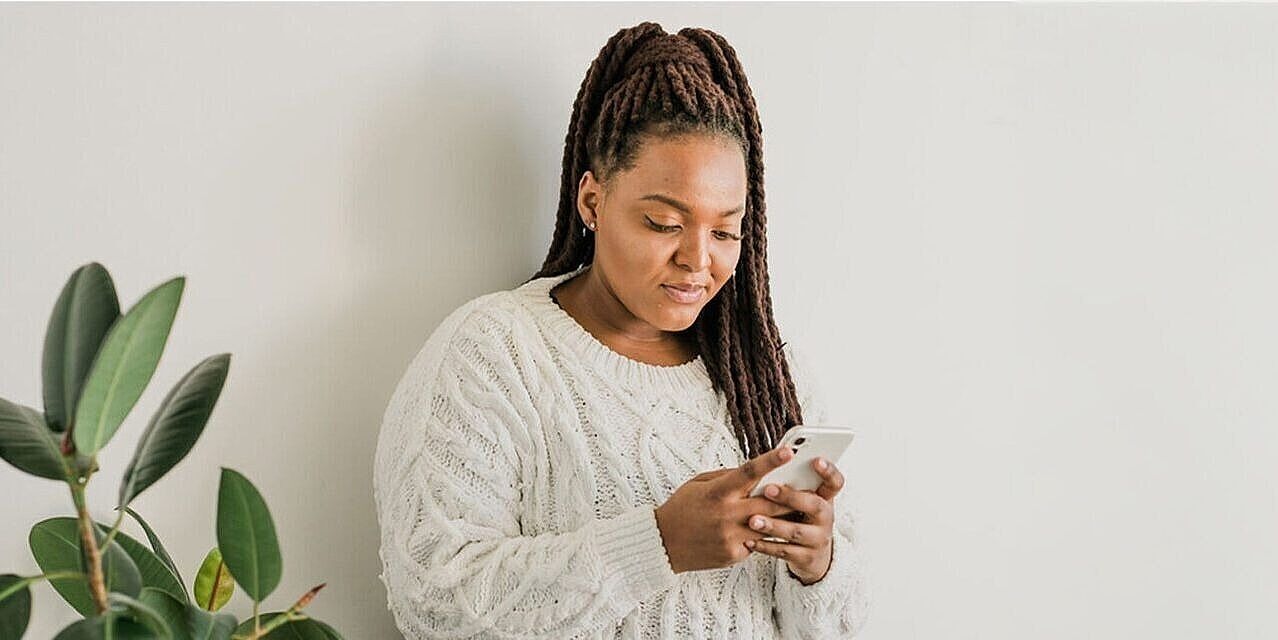 Eine Frau sieht auf ihr Smartphone, im Hintergrund eine Pflanze