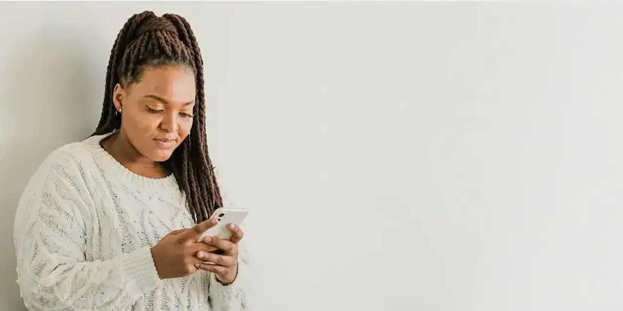 Eine Frau sieht auf ihr Smartphone, im Hintergrund eine Pflanze