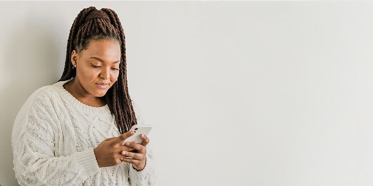 Eine Frau sieht auf ihr Smartphone, im Hintergrund eine Pflanze