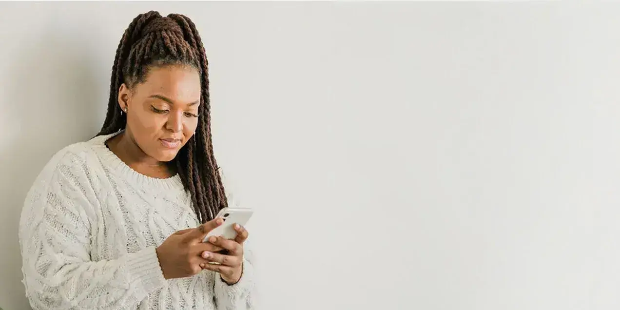 Eine Frau sieht auf ihr Smartphone, im Hintergrund eine Pflanze