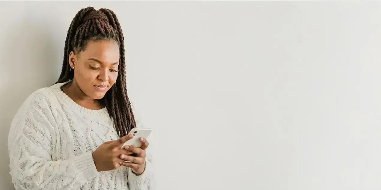 Eine Frau sieht auf ihr Smartphone, im Hintergrund eine Pflanze