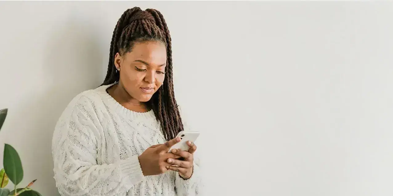 Eine Frau sieht auf ihr Smartphone, im Hintergrund eine Pflanze