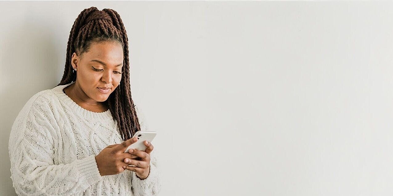 Eine Frau sieht auf ihr Smartphone, im Hintergrund eine Pflanze