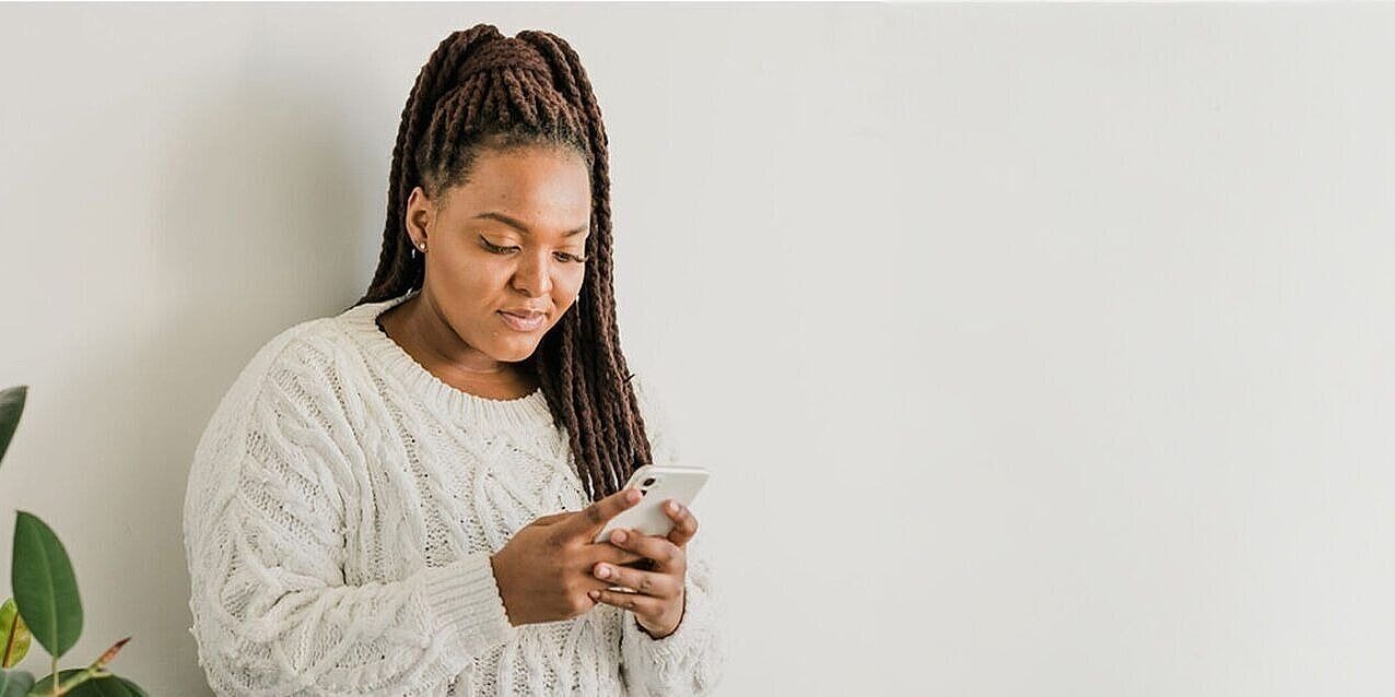 Eine Frau sieht auf ihr Smartphone, im Hintergrund eine Pflanze