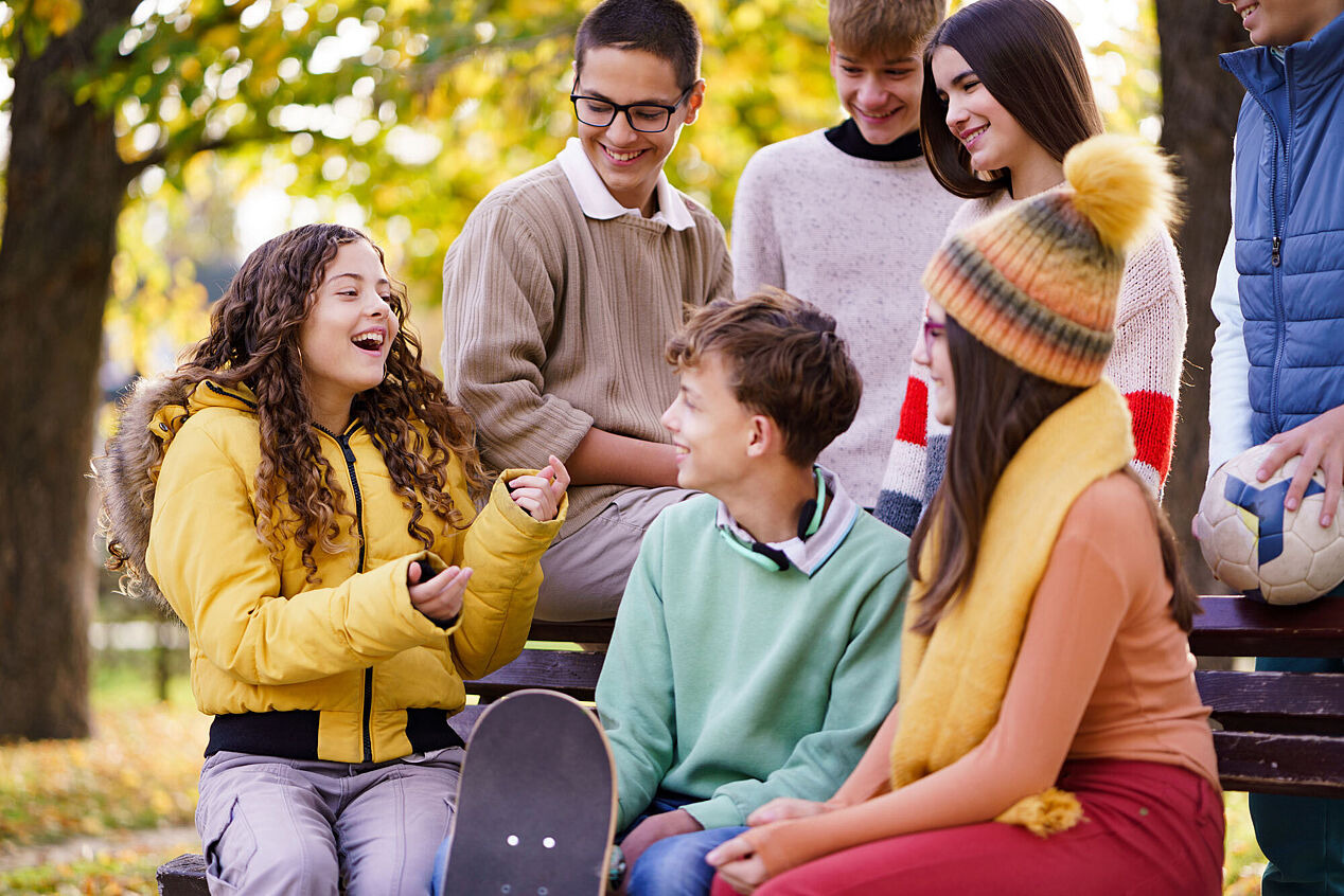 Gruppe von sitzenden und stehenden Jugendlichen vor Bäumen