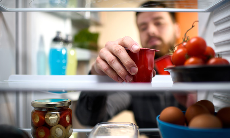 Männliche Person nimmt einen Plastikbecher aus dem Kühlschrank