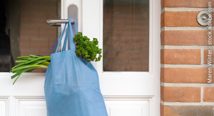 Einkaufsbeutel mit Gemüse hängt außen an der Haustürklinke