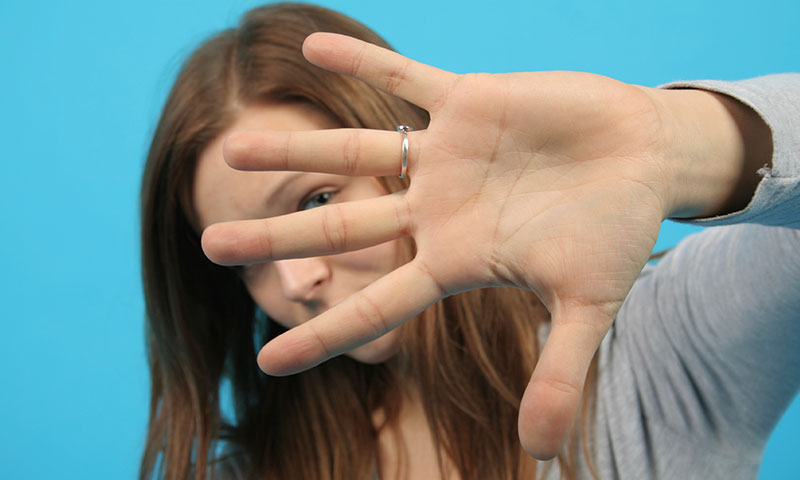 Frau hält sich abwährend die Hand vor ihr Gesicht (© iStock.com / arfo)